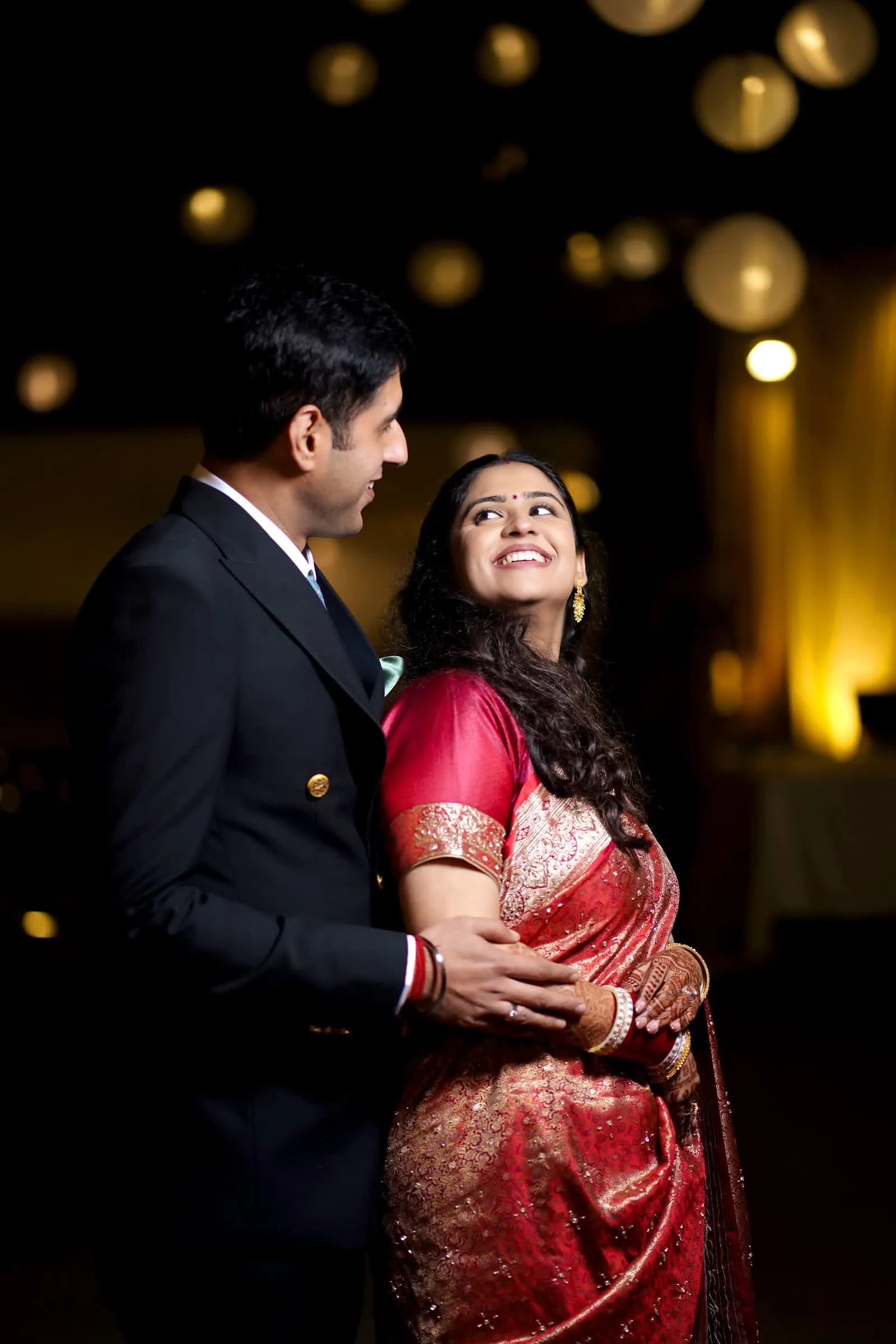 Couple embracing under warm bokeh lights at their wedding reception