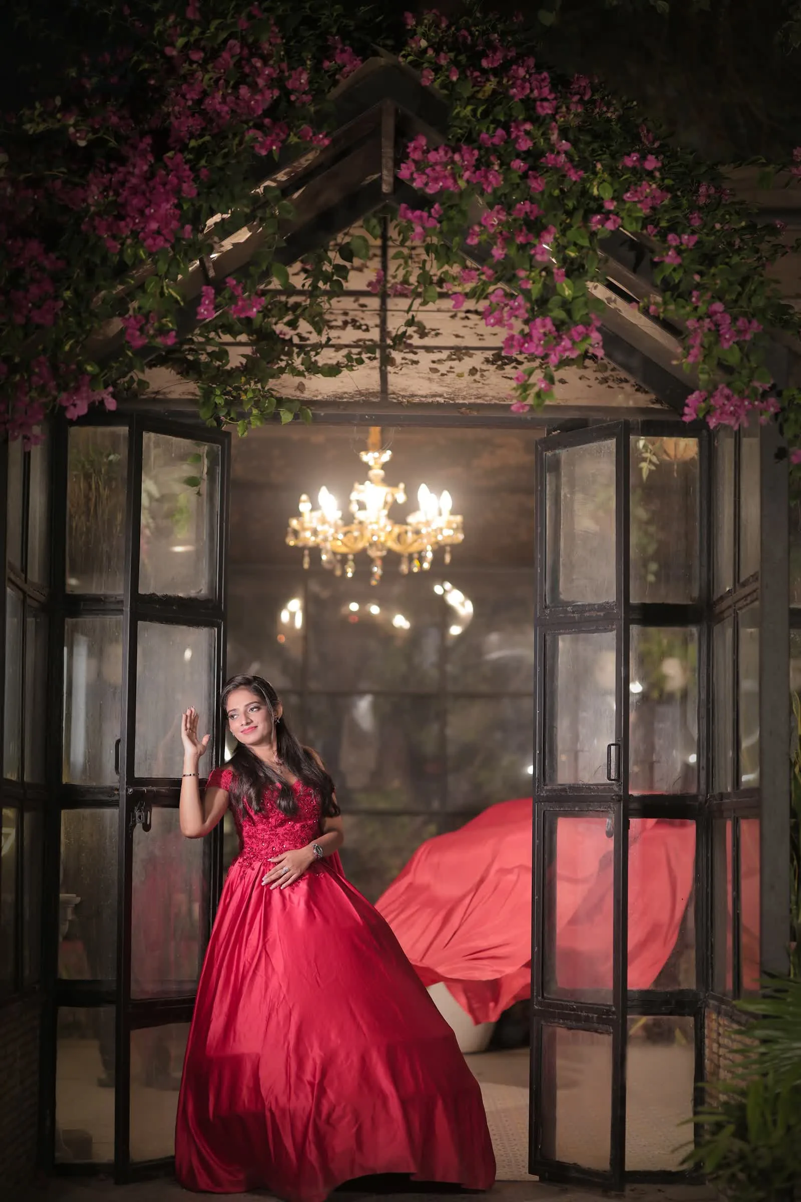 Woman in a red gown inside a glasshouse lit by a chandelier, Delhi pre-wedding shoot